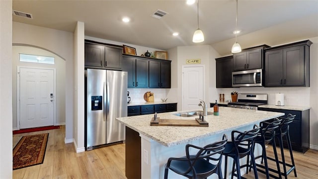 kitchen featuring tasteful backsplash, sink, stainless steel appliances, light stone countertops, and a center island with sink