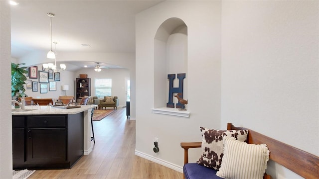 kitchen featuring sink, vaulted ceiling, hanging light fixtures, light wood-type flooring, and ceiling fan with notable chandelier