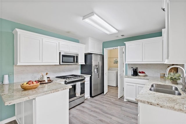 kitchen featuring a sink, washer / clothes dryer, white cabinetry, stainless steel appliances, and a peninsula