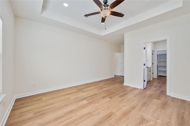 unfurnished bedroom featuring a raised ceiling, a walk in closet, light hardwood / wood-style flooring, ceiling fan, and a closet