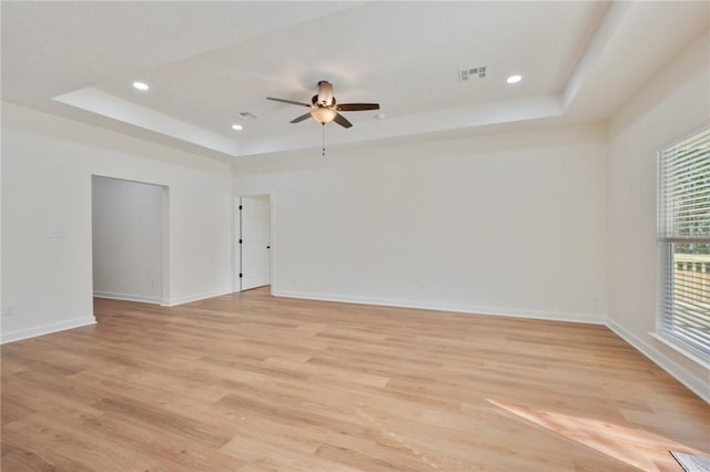 unfurnished room with a raised ceiling, ceiling fan, and light hardwood / wood-style flooring