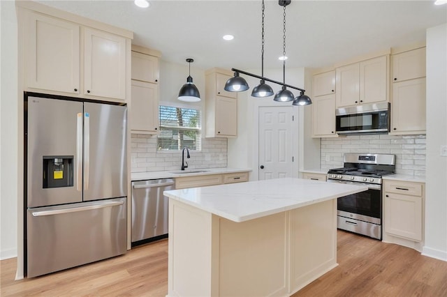 kitchen with appliances with stainless steel finishes, light wood-type flooring, sink, decorative light fixtures, and a center island