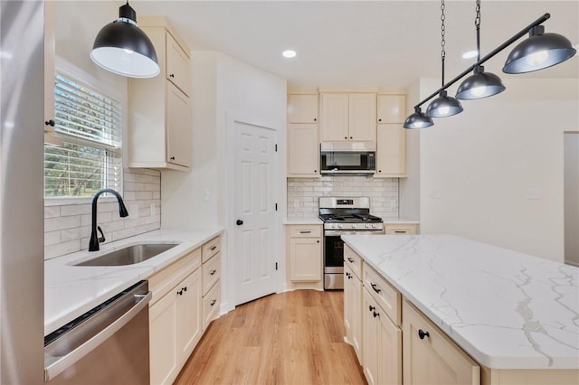 kitchen with sink, hanging light fixtures, decorative backsplash, light hardwood / wood-style floors, and stainless steel appliances