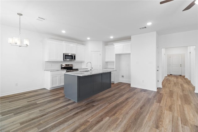 kitchen with sink, stainless steel appliances, an island with sink, white cabinets, and ceiling fan with notable chandelier