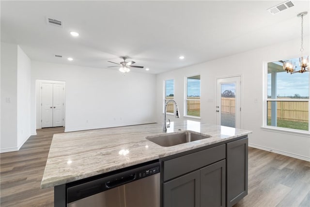 kitchen with light stone counters, stainless steel dishwasher, ceiling fan with notable chandelier, sink, and pendant lighting