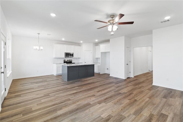 kitchen featuring an island with sink, decorative light fixtures, white cabinets, ceiling fan with notable chandelier, and appliances with stainless steel finishes