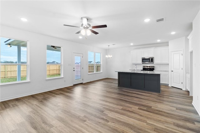 kitchen featuring white cabinetry, tasteful backsplash, a kitchen island with sink, ceiling fan with notable chandelier, and appliances with stainless steel finishes