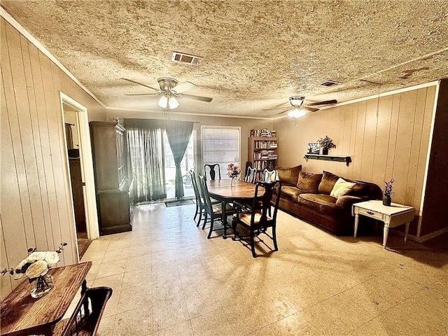 dining room with ceiling fan, a textured ceiling, and wooden walls