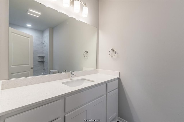 bathroom featuring toilet, tiled shower, and vanity