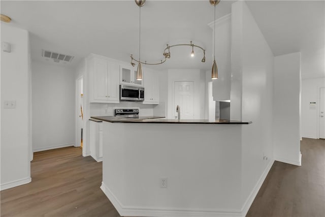 kitchen featuring white cabinets, decorative light fixtures, stainless steel appliances, and hardwood / wood-style floors