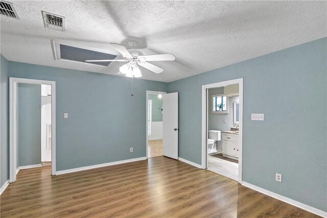 unfurnished bedroom featuring connected bathroom, ceiling fan, dark hardwood / wood-style flooring, and a textured ceiling