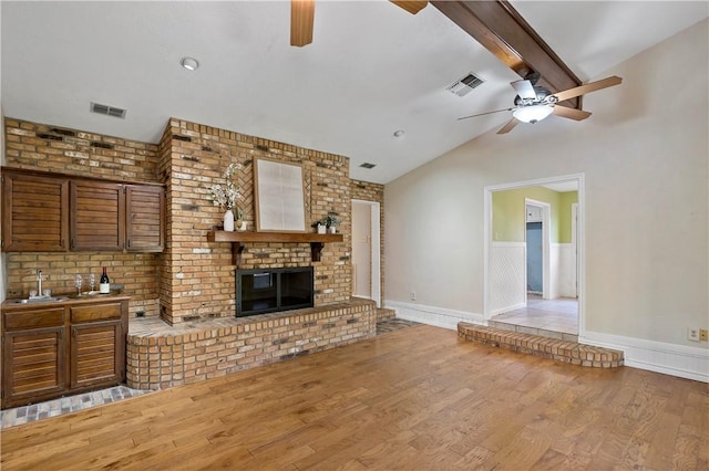 living room with ceiling fan, sink, lofted ceiling with beams, light hardwood / wood-style floors, and a fireplace