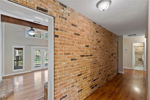 hallway featuring wood-type flooring, a textured ceiling, and brick wall