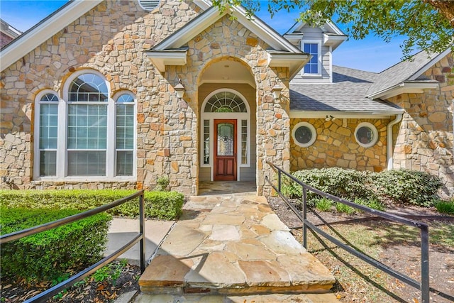 view of exterior entry featuring stone siding and roof with shingles