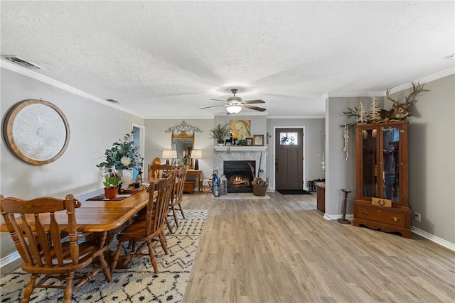 dining area with a textured ceiling, a lit fireplace, ornamental molding, and light wood-style floors