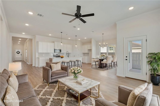 living room featuring ceiling fan with notable chandelier, crown molding, sink, and light hardwood / wood-style flooring