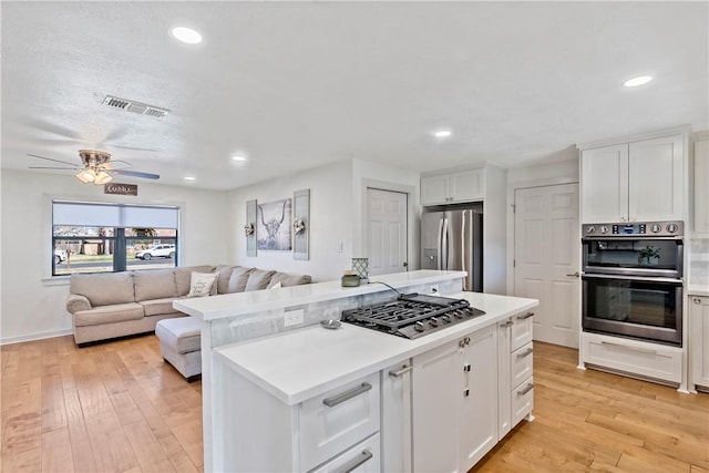 kitchen featuring appliances with stainless steel finishes, white cabinetry, visible vents, and a center island