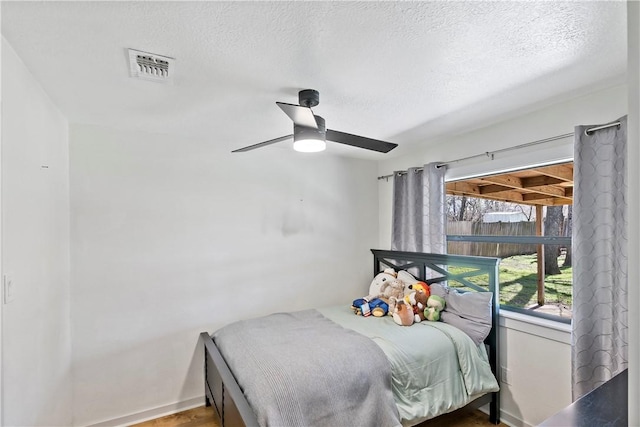 bedroom with a textured ceiling, visible vents, and a ceiling fan