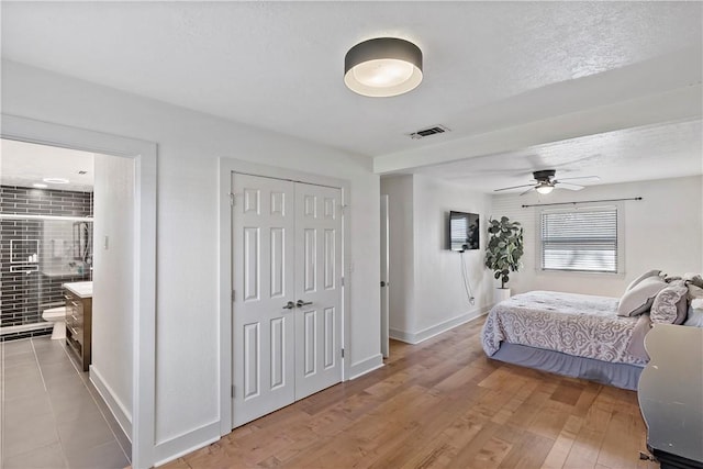 bedroom featuring connected bathroom, visible vents, baseboards, light wood-style floors, and a closet