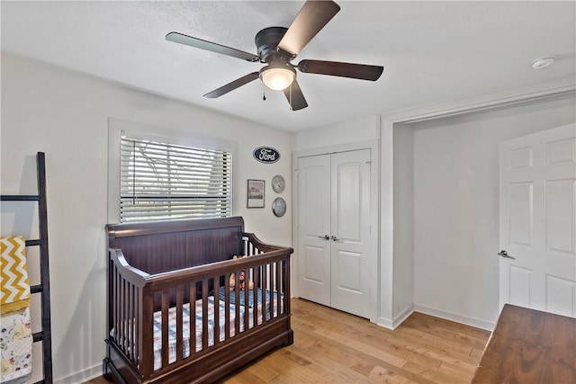 bedroom with a ceiling fan, baseboards, a closet, a nursery area, and light wood finished floors