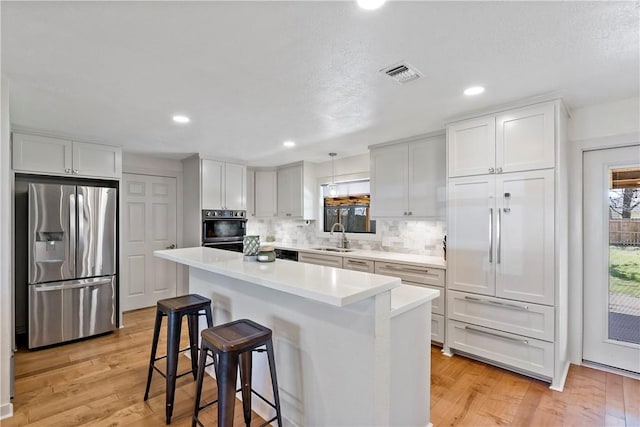 kitchen with appliances with stainless steel finishes, visible vents, light wood-style floors, and backsplash