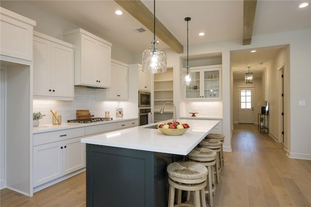 kitchen with beamed ceiling, light hardwood / wood-style floors, white cabinetry, and a kitchen island with sink