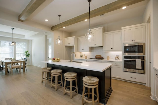 kitchen with white cabinetry, sink, beamed ceiling, a kitchen island with sink, and appliances with stainless steel finishes