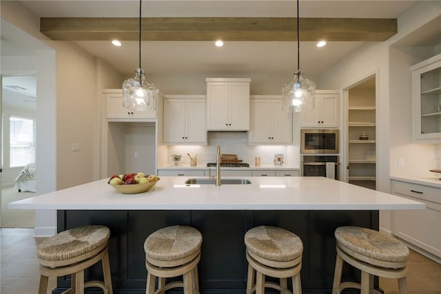 kitchen featuring oven, sink, an island with sink, built in microwave, and beamed ceiling