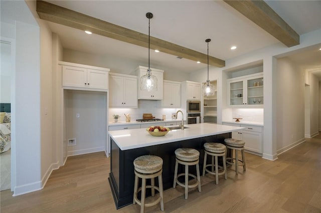 kitchen featuring beam ceiling, backsplash, white cabinetry, and a center island with sink