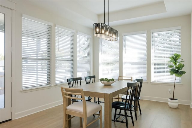 dining area with a raised ceiling, light wood-type flooring, and an inviting chandelier