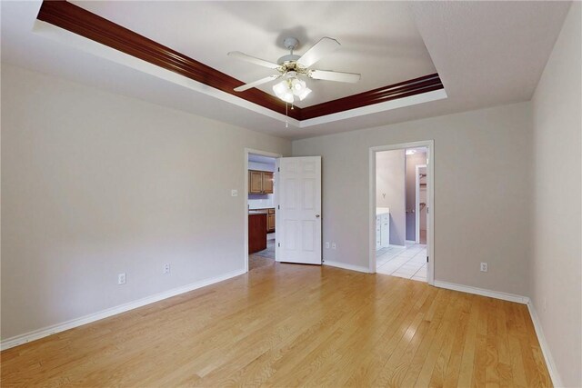 2600 Greenberry Cir, College Station, TX 77845 - unfurnished bedroom featuring a tray ceiling, light wood-style floors, baseboards, connected bathroom, and ceiling fan