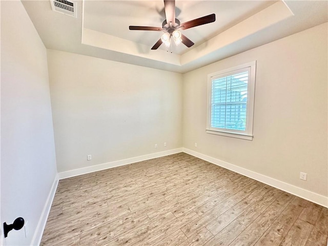 empty room with ceiling fan, light wood-type flooring, and a tray ceiling