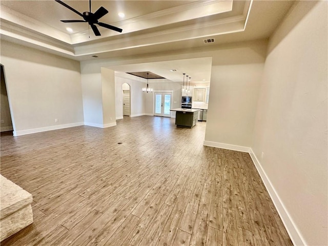 unfurnished living room with wood-type flooring, a raised ceiling, ceiling fan, and ornamental molding