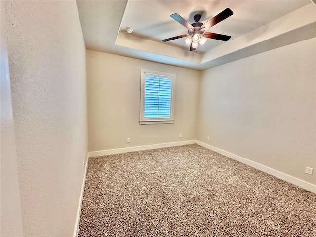 empty room featuring carpet, a tray ceiling, and ceiling fan