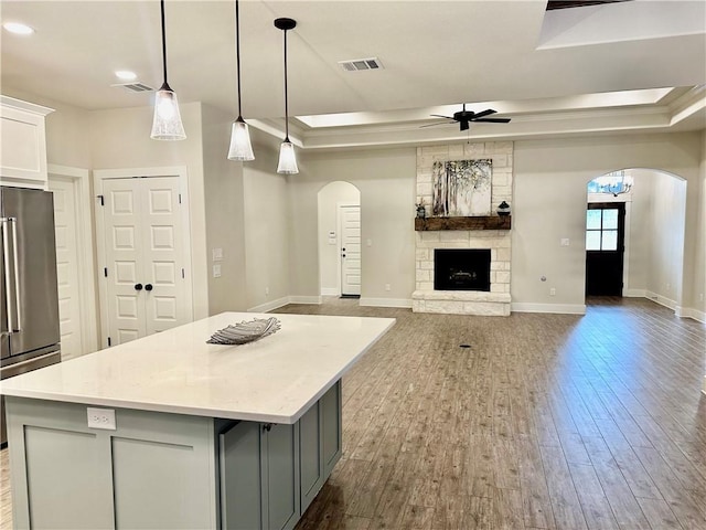 kitchen with pendant lighting, ceiling fan with notable chandelier, a stone fireplace, stainless steel fridge, and a kitchen island