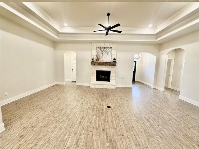 unfurnished living room with a fireplace, wood-type flooring, a tray ceiling, and ceiling fan