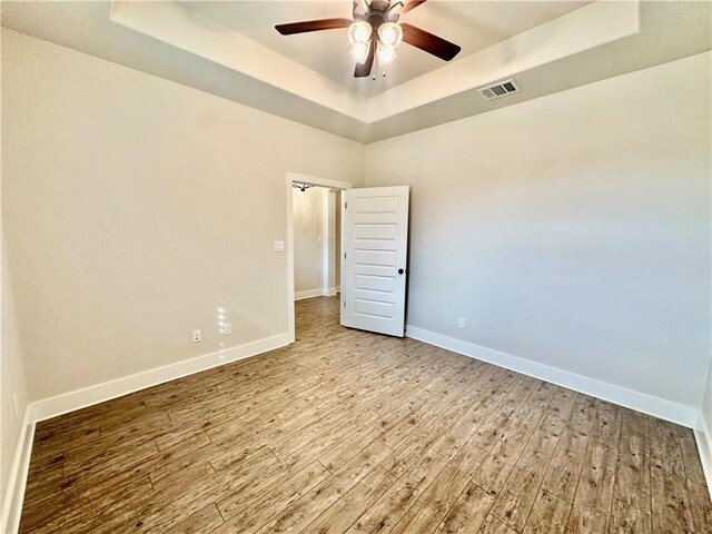 spare room with a raised ceiling, ceiling fan, and light wood-type flooring