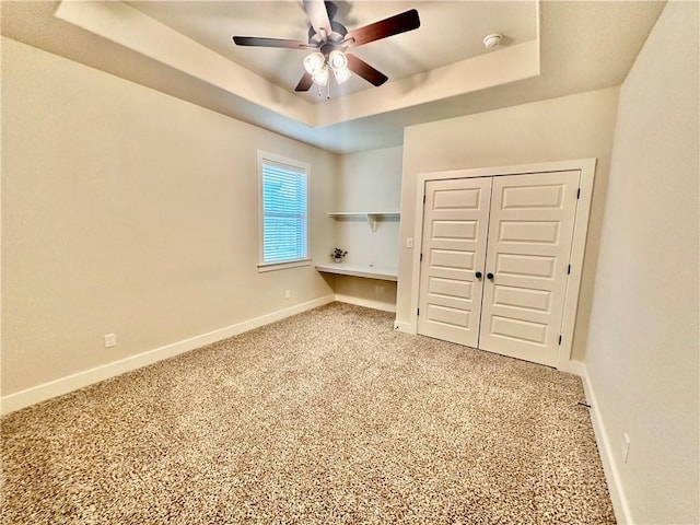 unfurnished bedroom with a raised ceiling, ceiling fan, a closet, and carpet floors