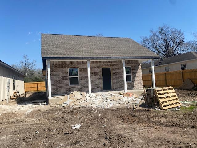 rear view of property with brick siding, roof with shingles, and fence