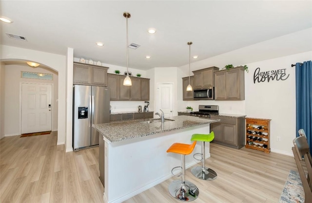 kitchen featuring a center island with sink, visible vents, arched walkways, appliances with stainless steel finishes, and hanging light fixtures