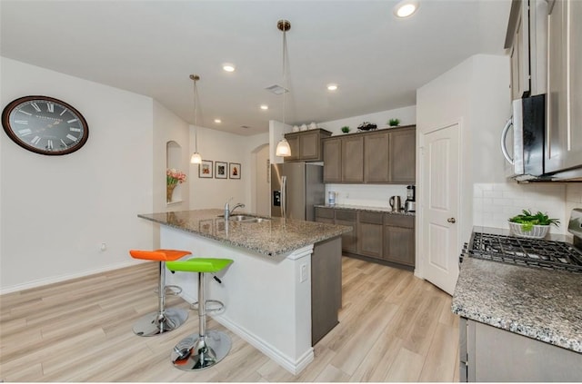 kitchen featuring stone counters, arched walkways, hanging light fixtures, appliances with stainless steel finishes, and light wood-style floors