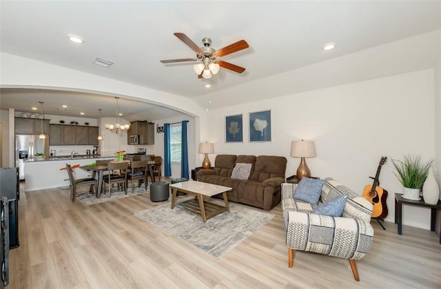 living room with arched walkways, visible vents, ceiling fan with notable chandelier, and light wood-style flooring