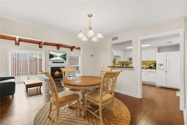 dining area with a notable chandelier, visible vents, dark wood-style floors, and a lit fireplace