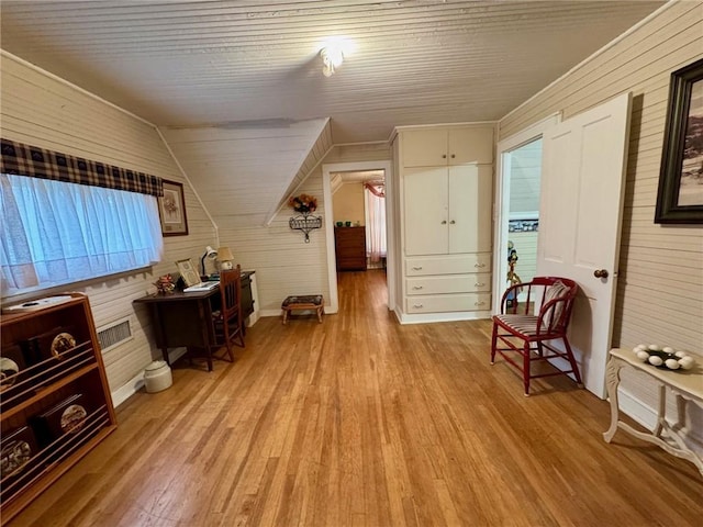 living area with wooden walls, vaulted ceiling, and light wood-type flooring