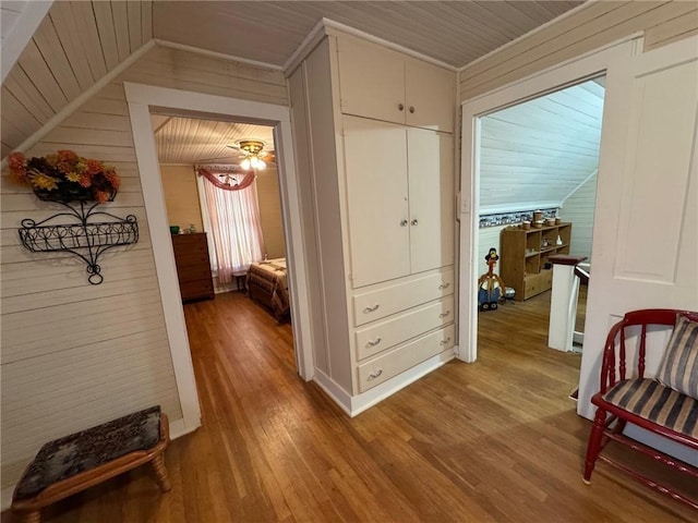 hallway featuring lofted ceiling, crown molding, wooden walls, and light hardwood / wood-style flooring