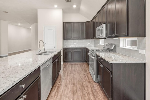 kitchen featuring appliances with stainless steel finishes, dark brown cabinets, sink, and light stone counters