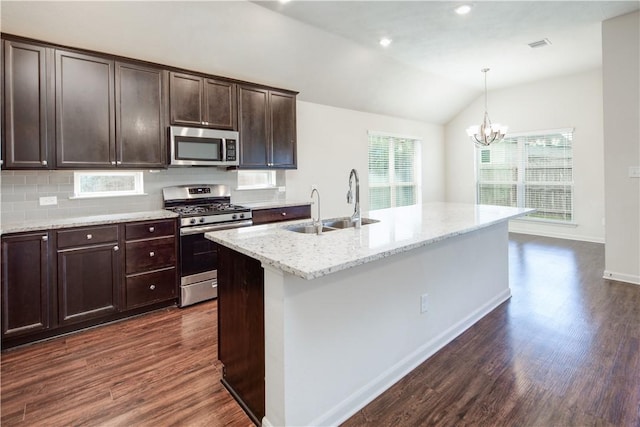 kitchen with stainless steel appliances, pendant lighting, a center island with sink, and light stone counters