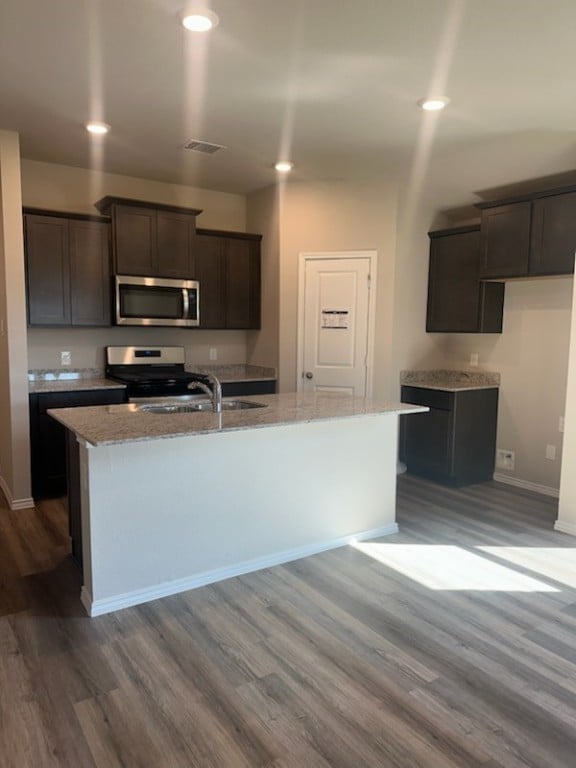 kitchen featuring sink, dark hardwood / wood-style floors, dark brown cabinets, a center island with sink, and range