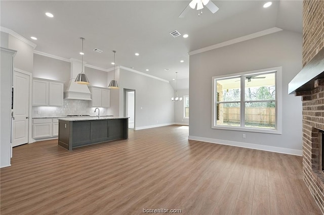 unfurnished living room with hardwood / wood-style flooring, vaulted ceiling, ornamental molding, and a brick fireplace