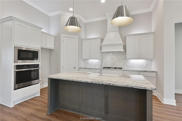 kitchen featuring light wood-type flooring, stainless steel appliances, a kitchen island with sink, pendant lighting, and white cabinets